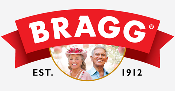 The Bragg logo features a bold red ribbon with the word “BRAGG” in white capital letters, arched above an oval photo of the founders, with “Est. 1912” displayed on either side, emphasizing heritage and longevity.