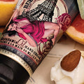 Barefoot Venus Ruby Red macadamia oil hand cream label details next to a white lotion swirl and almond nut.